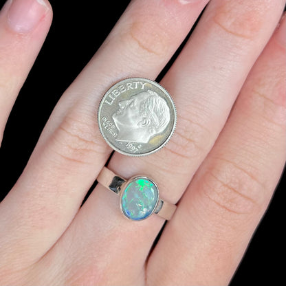 A sterling silver Lightning Ridge opal solitaire ring, worn on a hand next to a US dime coin for scale.