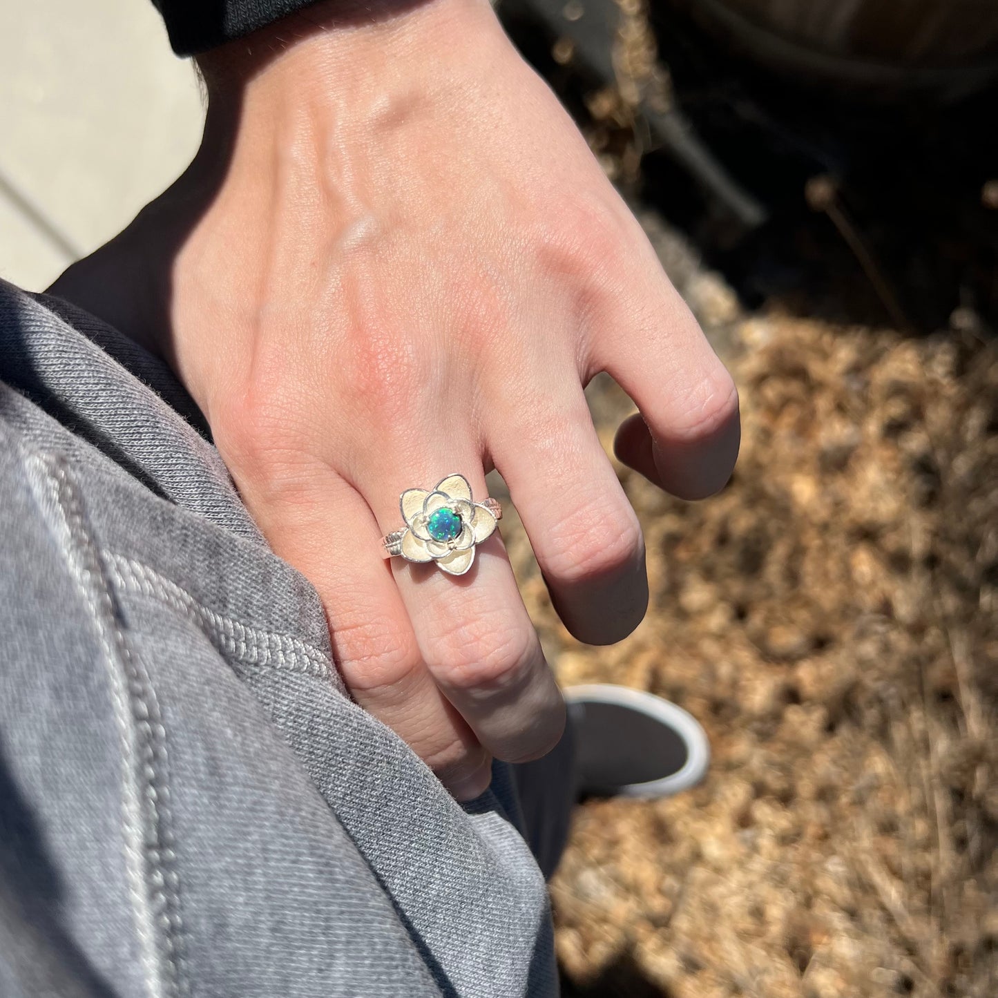 Person resting hand on hip in sunlight while wearing a sterling silver lotus flower ring set with a round Australian black opal