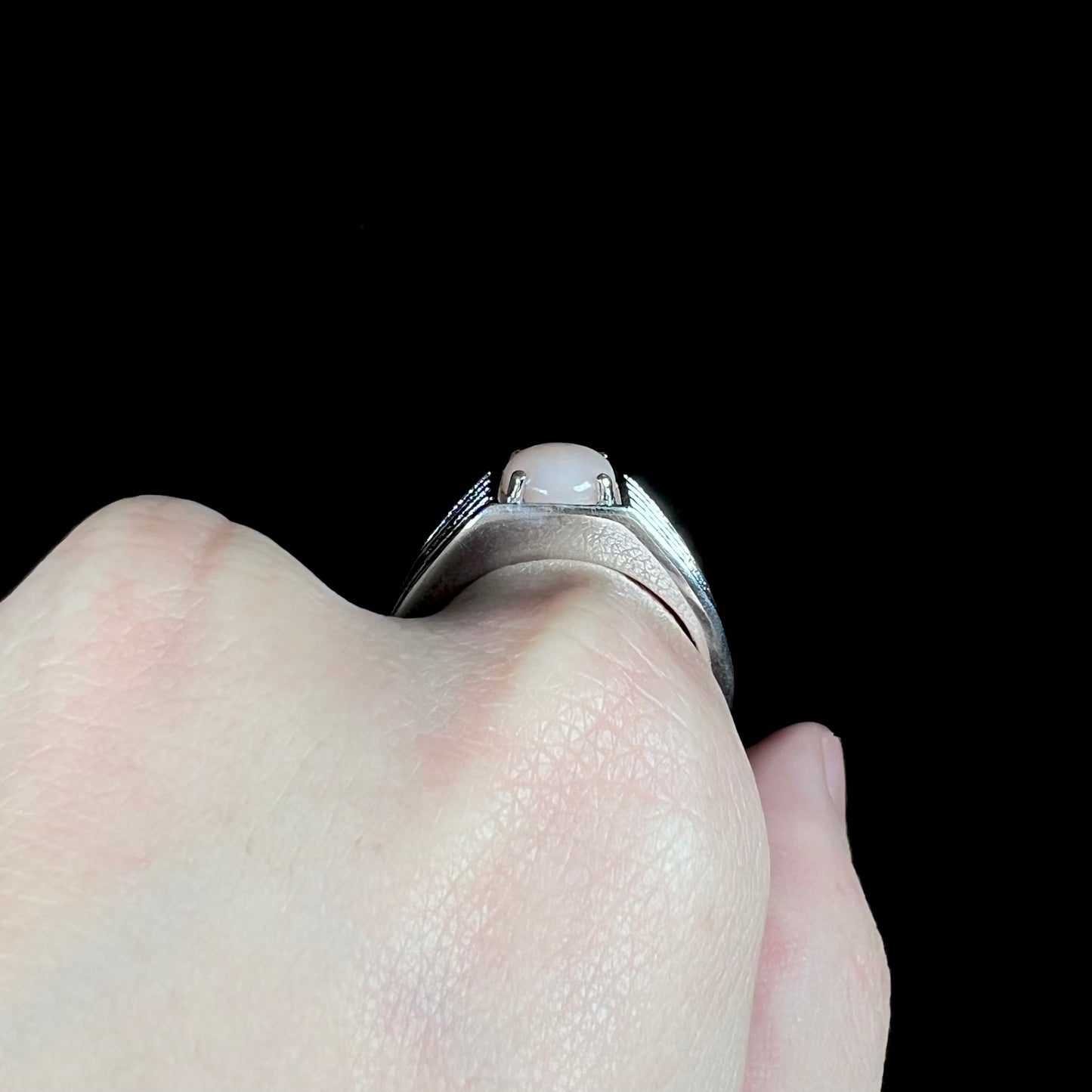 A sterling silver men's pink opal ring on hand shown from side profile view