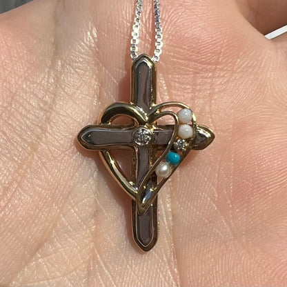 A two-tone sterling silver mother's cross necklace set with diamond, opal, turquoise, and pearl, shown in sunlight.