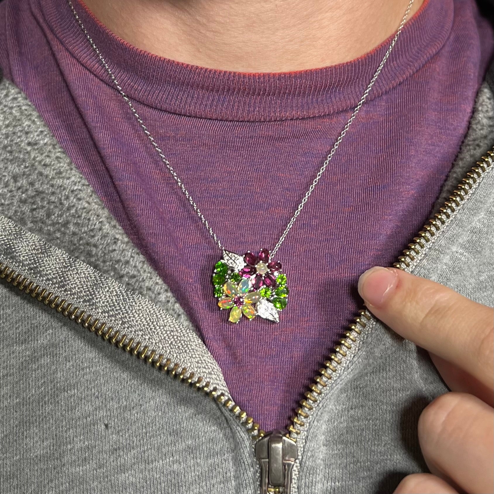 A sterling silver opal and garnet flower necklace shown worn around a neck against a purple shirt.