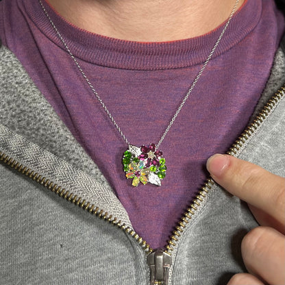 A sterling silver opal and garnet flower necklace shown worn around a neck against a purple shirt.