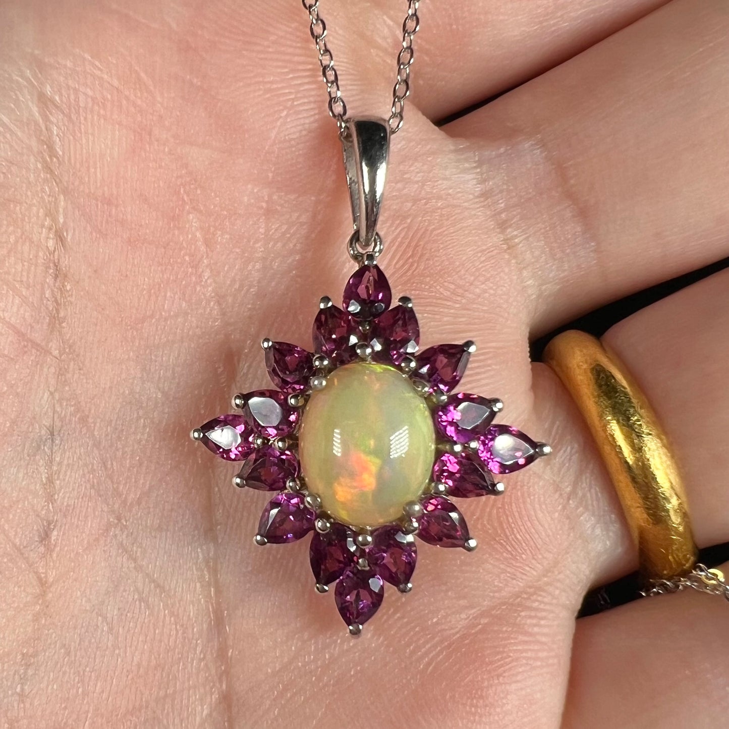 A sterling silver Ethiopian opal and rhodolite garnet spray necklace shown close-up in a hand.