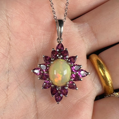 A sterling silver Ethiopian opal and rhodolite garnet spray necklace shown close-up in a hand.