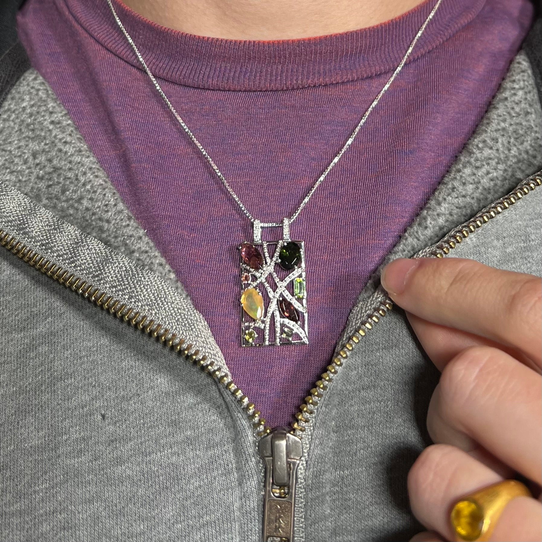 A silver multi-stone necklace set with Ethiopian opal, tourmaline, and diamonds, worn over a purple shirt.
