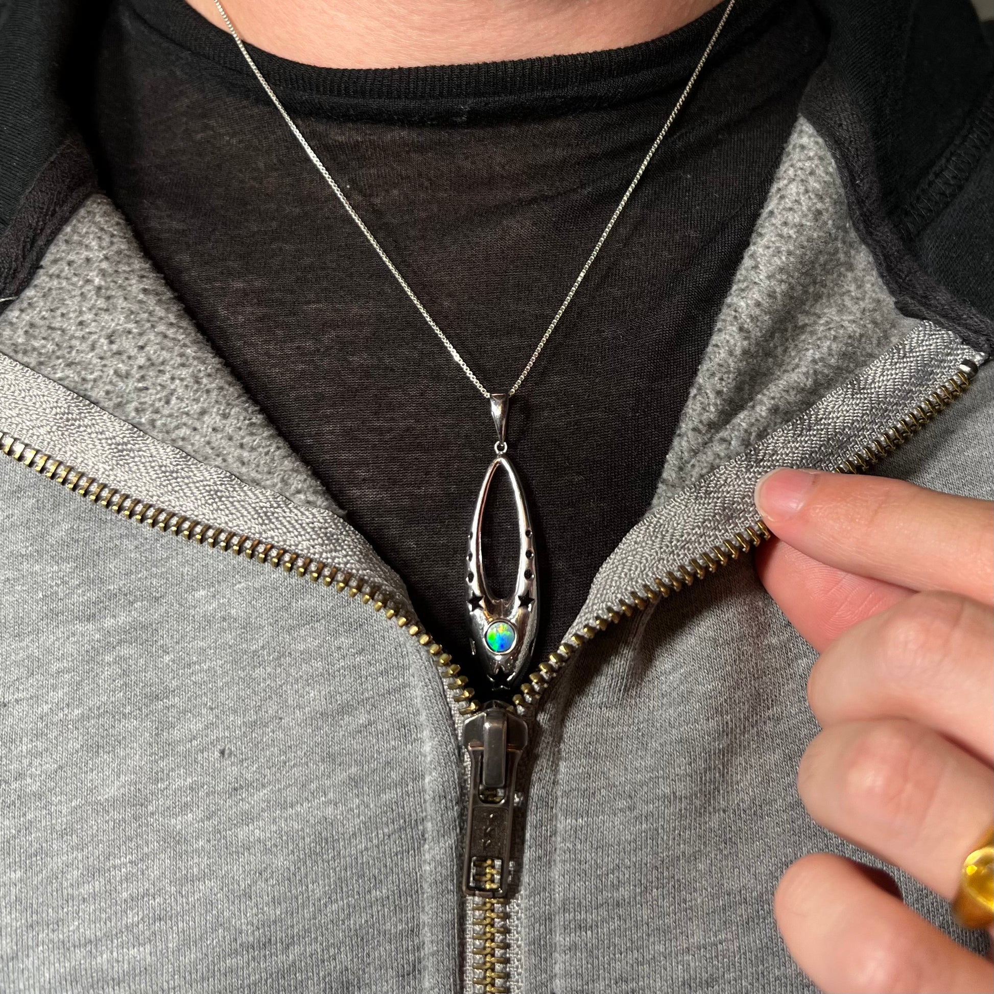 A sterling silver and opal doublet ballerina shoe necklace worn around a neck against a dark shirt.