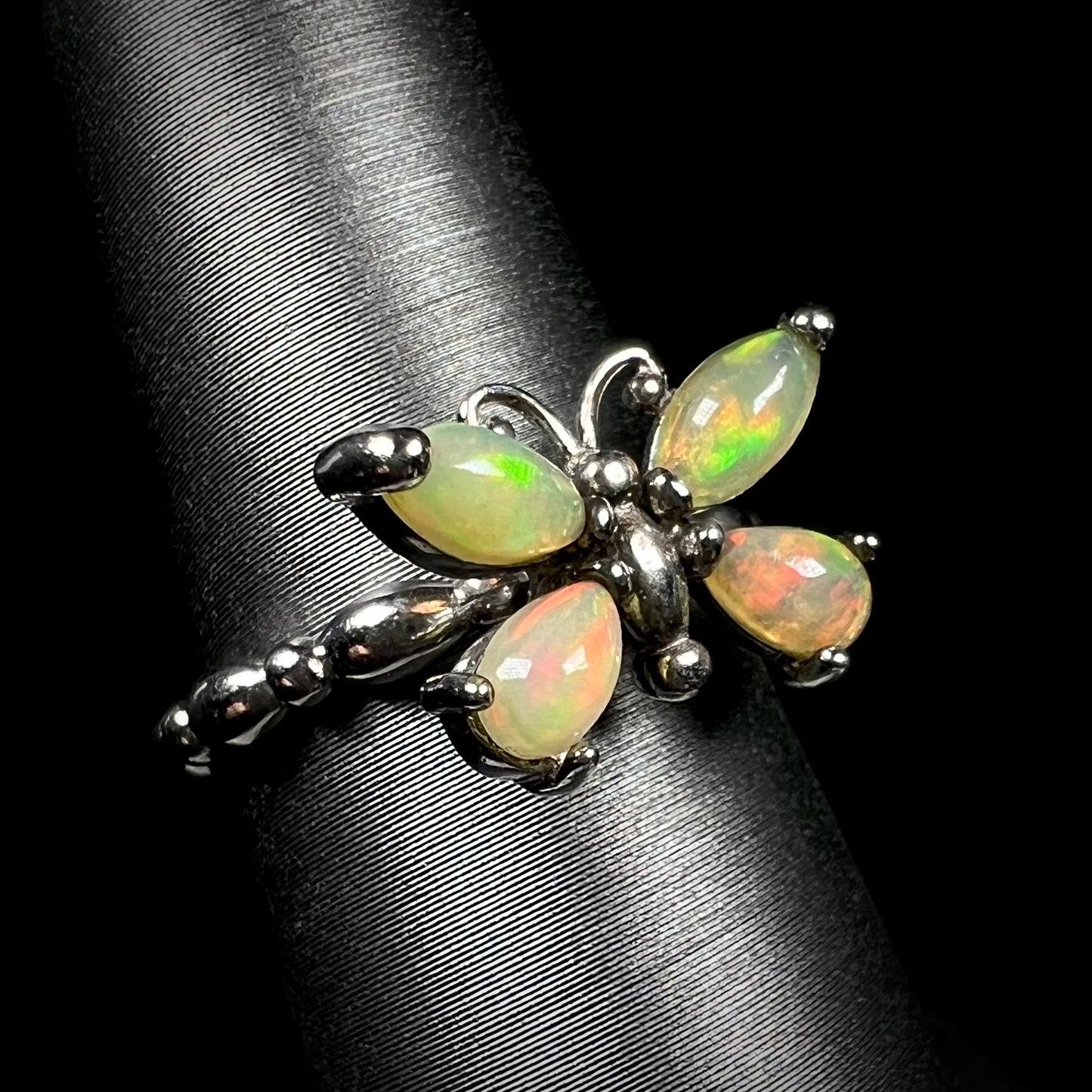 A sterling silver Ethiopian opal butterfly ring shown on a ring display at an angle against a black background.