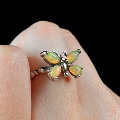 A sterling silver Ethiopian opal butterfly ring shown close-up at an angle on a finger against a black background.