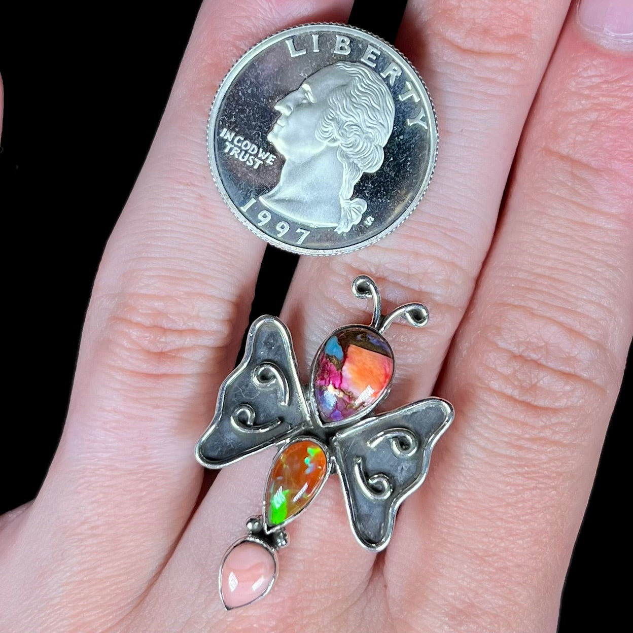 A sterling silver opal butterfly ring worn on a hand next to a 1997 S quarter coin for scale.
