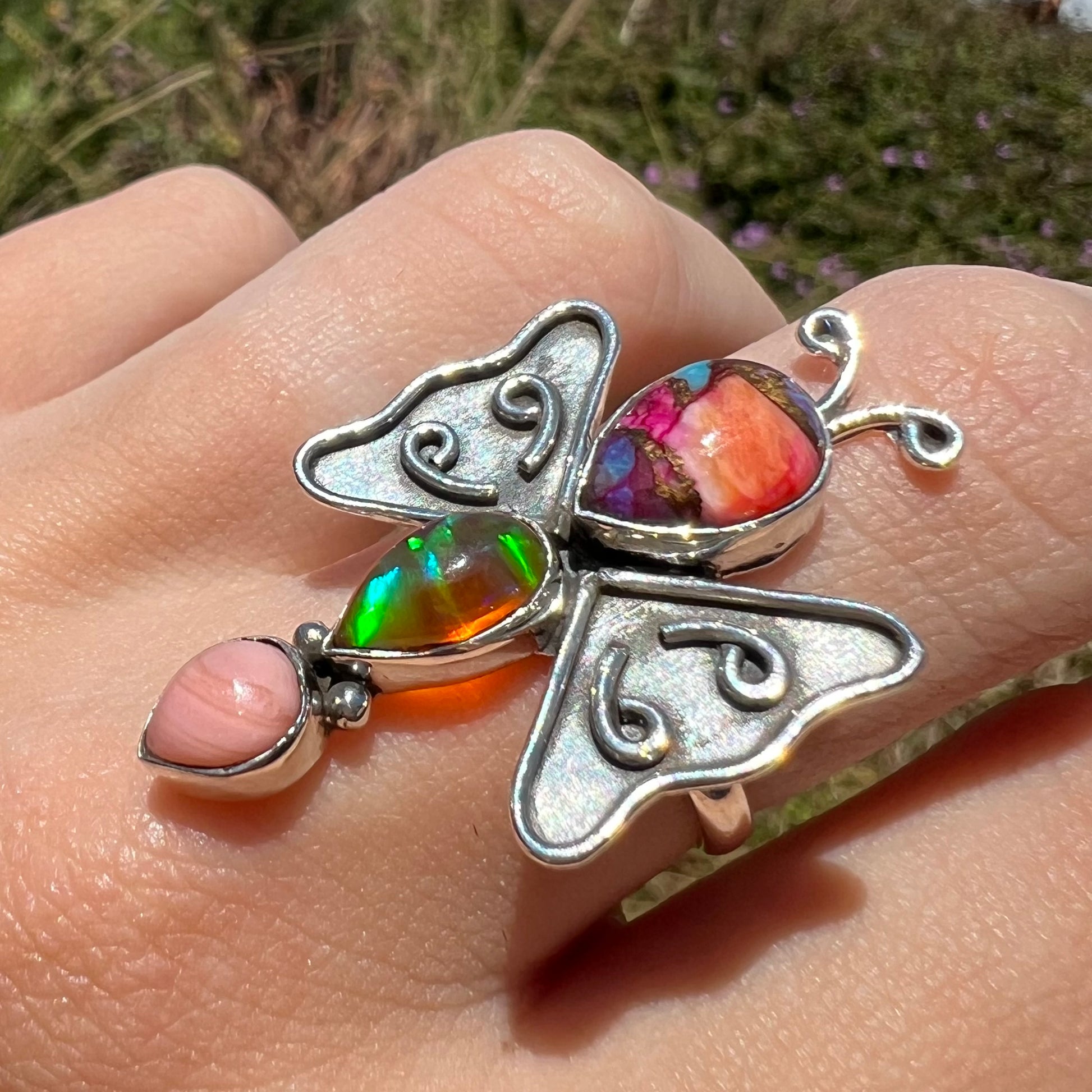 A sterling silver opal butterfly ring shown on a hand at an angle in natural sunlight.