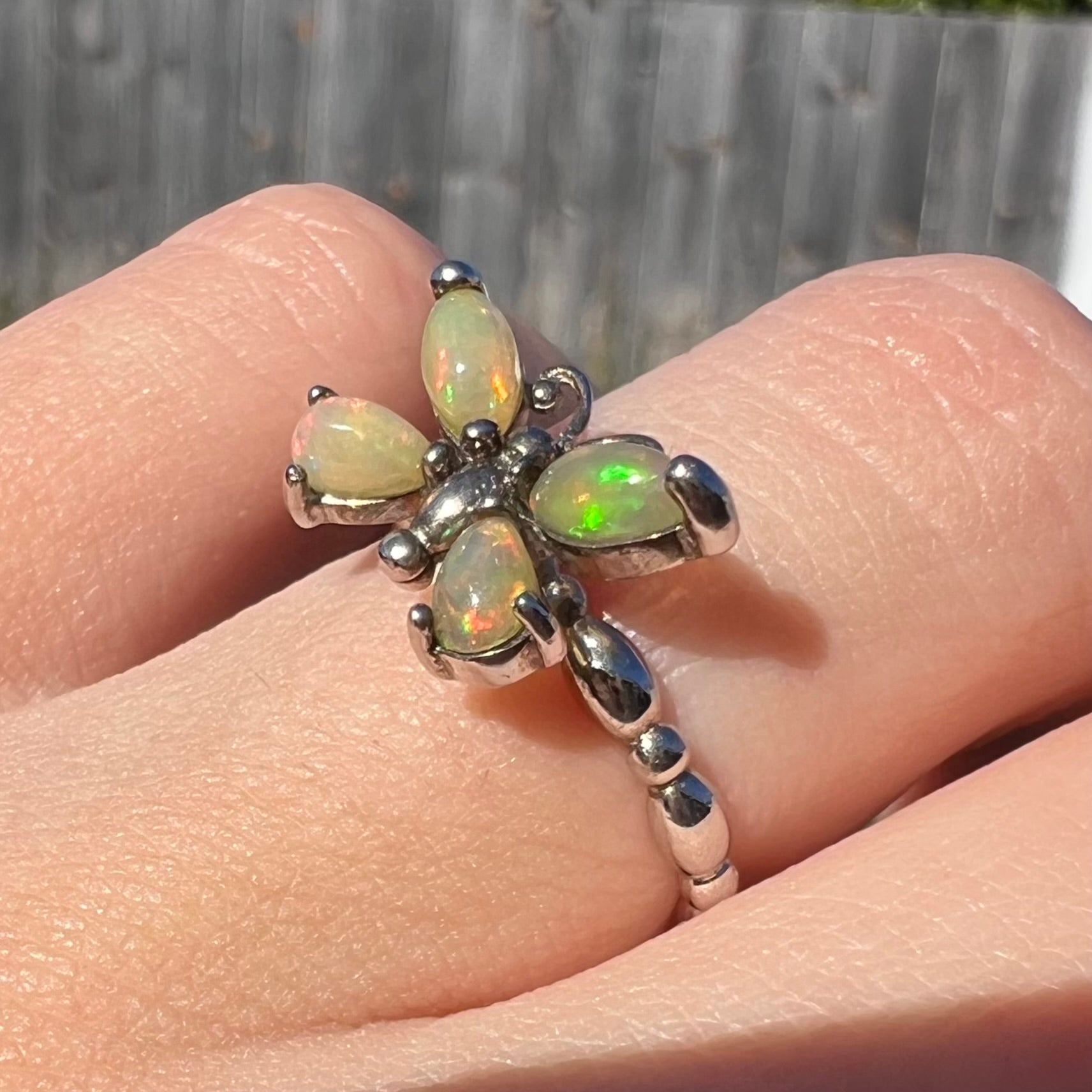 Close-up angled view of a sterling silver Ethiopian opal butterfly ring worn on a finger in sunlight.