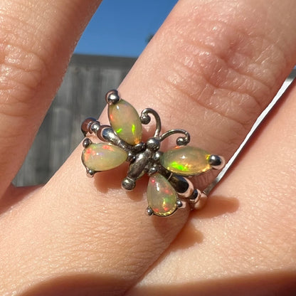 The front view of a sterling silver Ethiopian opal butterfly ring shown close-up on a finger in the sunlight.