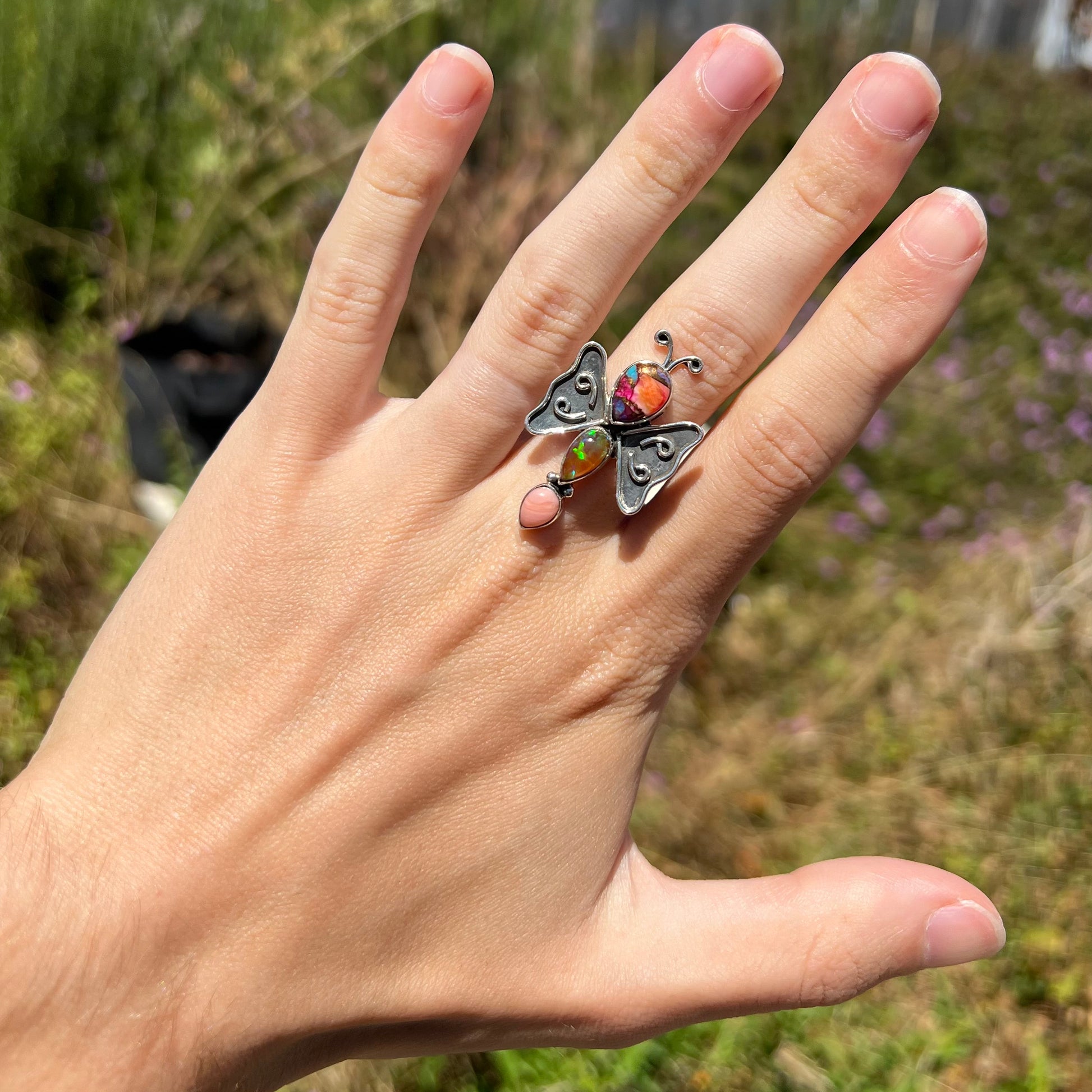 A handmade silver opal butterfly ring worn on a hand, shown in the sunlight at a distance.
