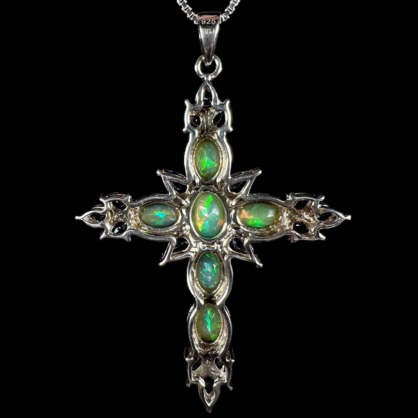 Back view of a sterling silver opal cross necklace against a black background.