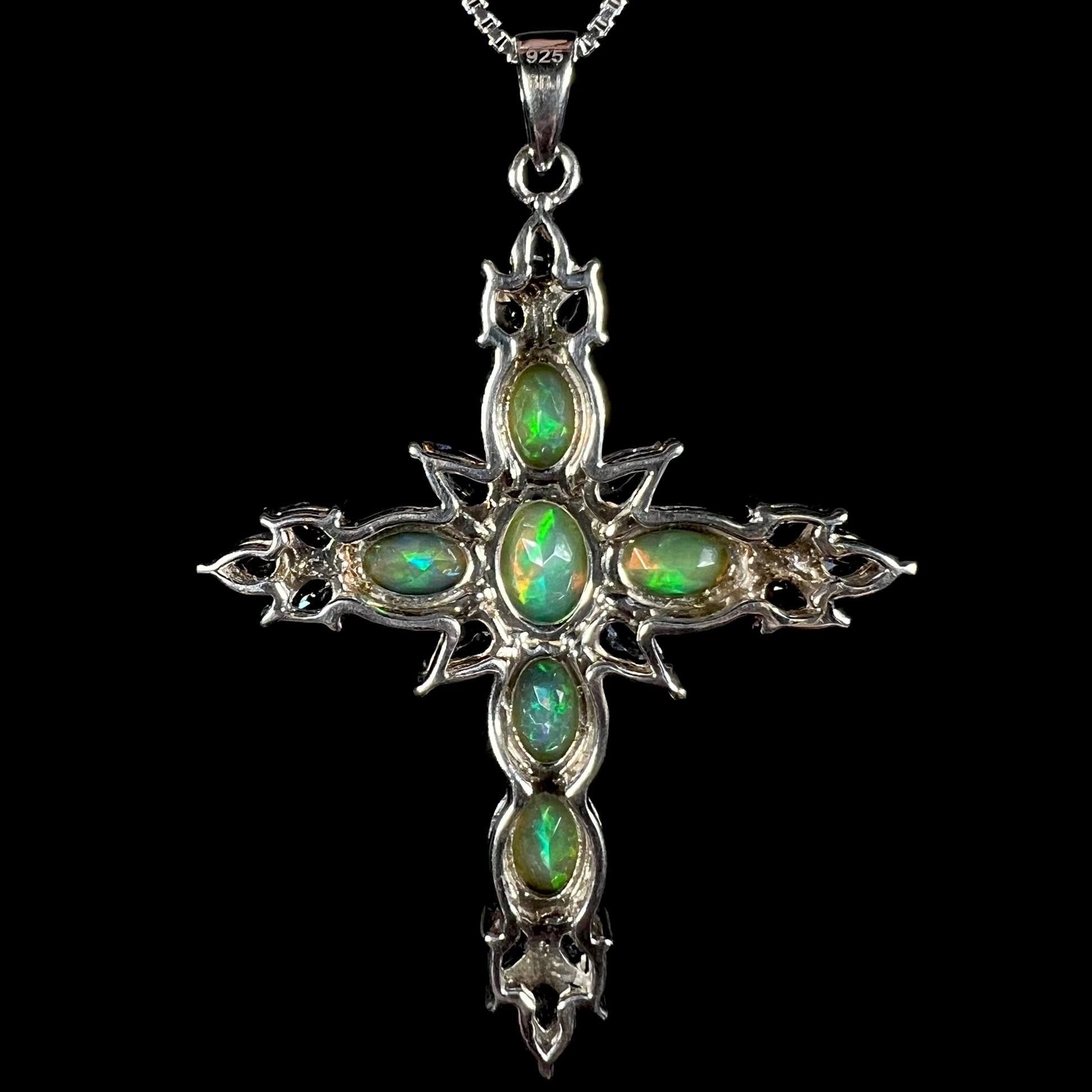 Back view of a sterling silver opal cross necklace against a black background.