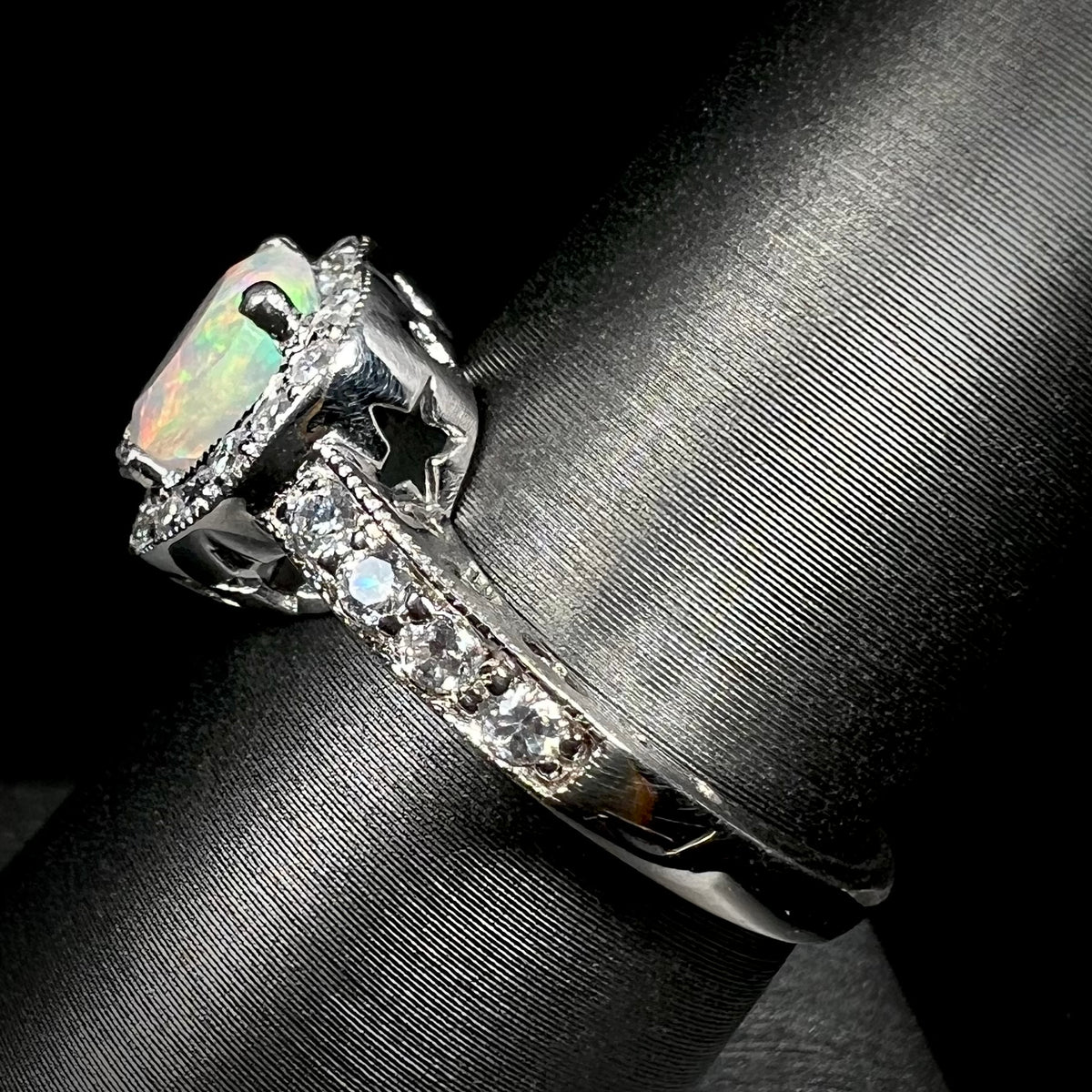 Side view of silver opal and cubic zirconia ring, viewing the ring from its shank; the ring has star shaped cutouts visible from beneth its gallery