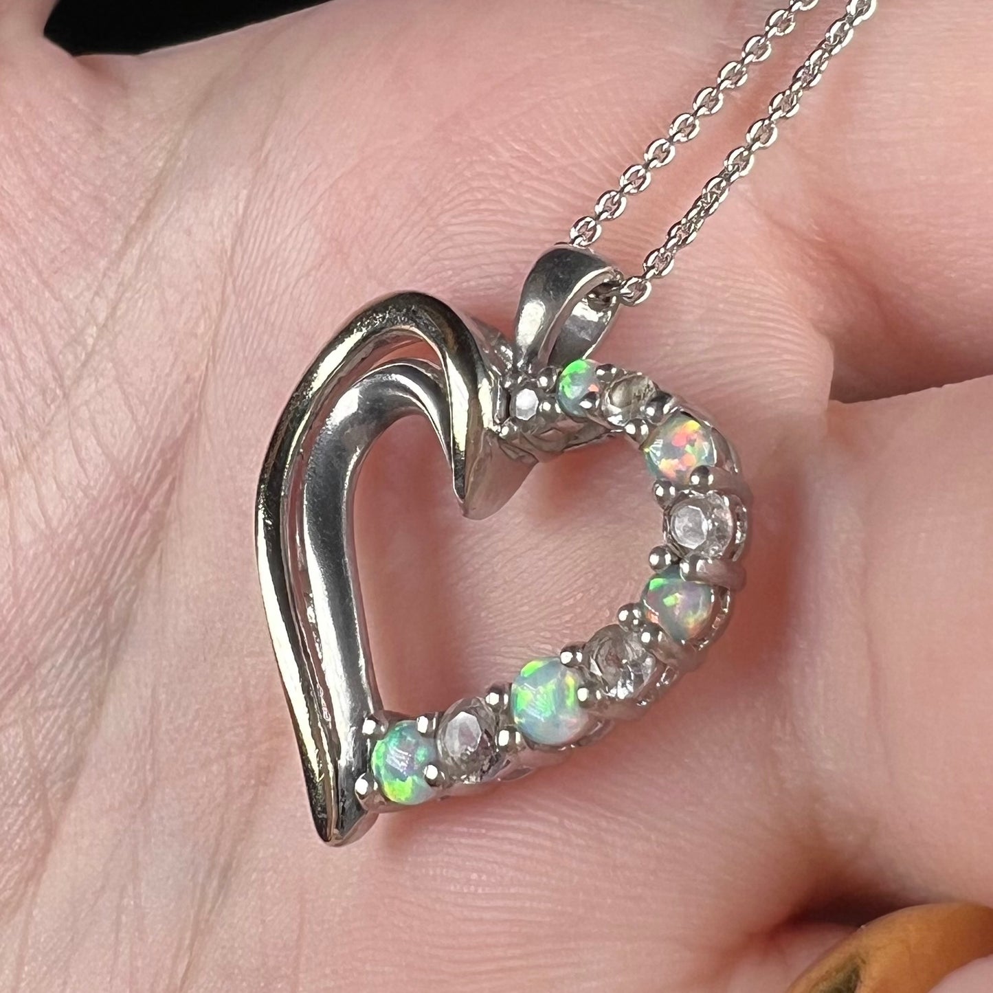 Angled close-up of a two-tone sterling silver and yellow gold lab-created opal and CZ heart necklace in a hand.