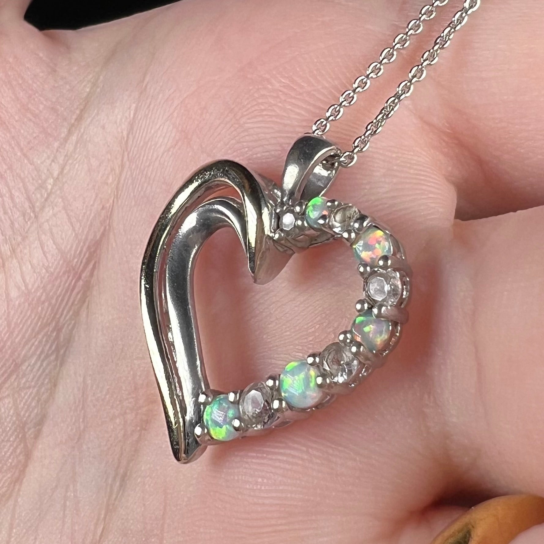 Angled close-up of a two-tone sterling silver and yellow gold lab-created opal and CZ heart necklace in a hand.