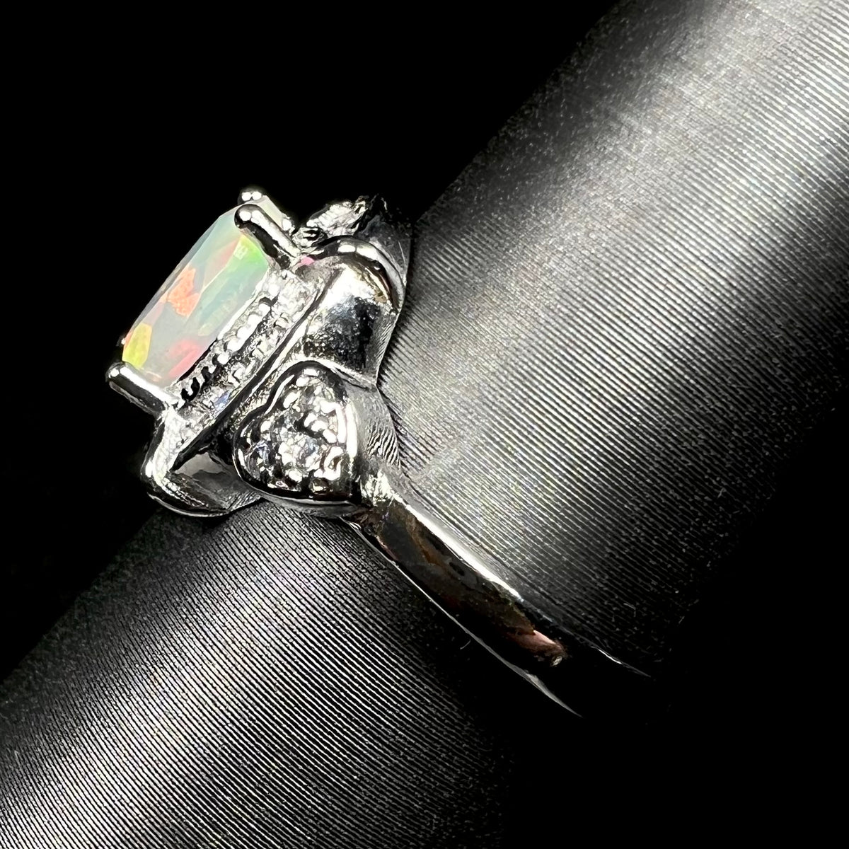 Side view of silver Ethiopian opal and cubic zirconia ring with heart design on display, showing ring's shank