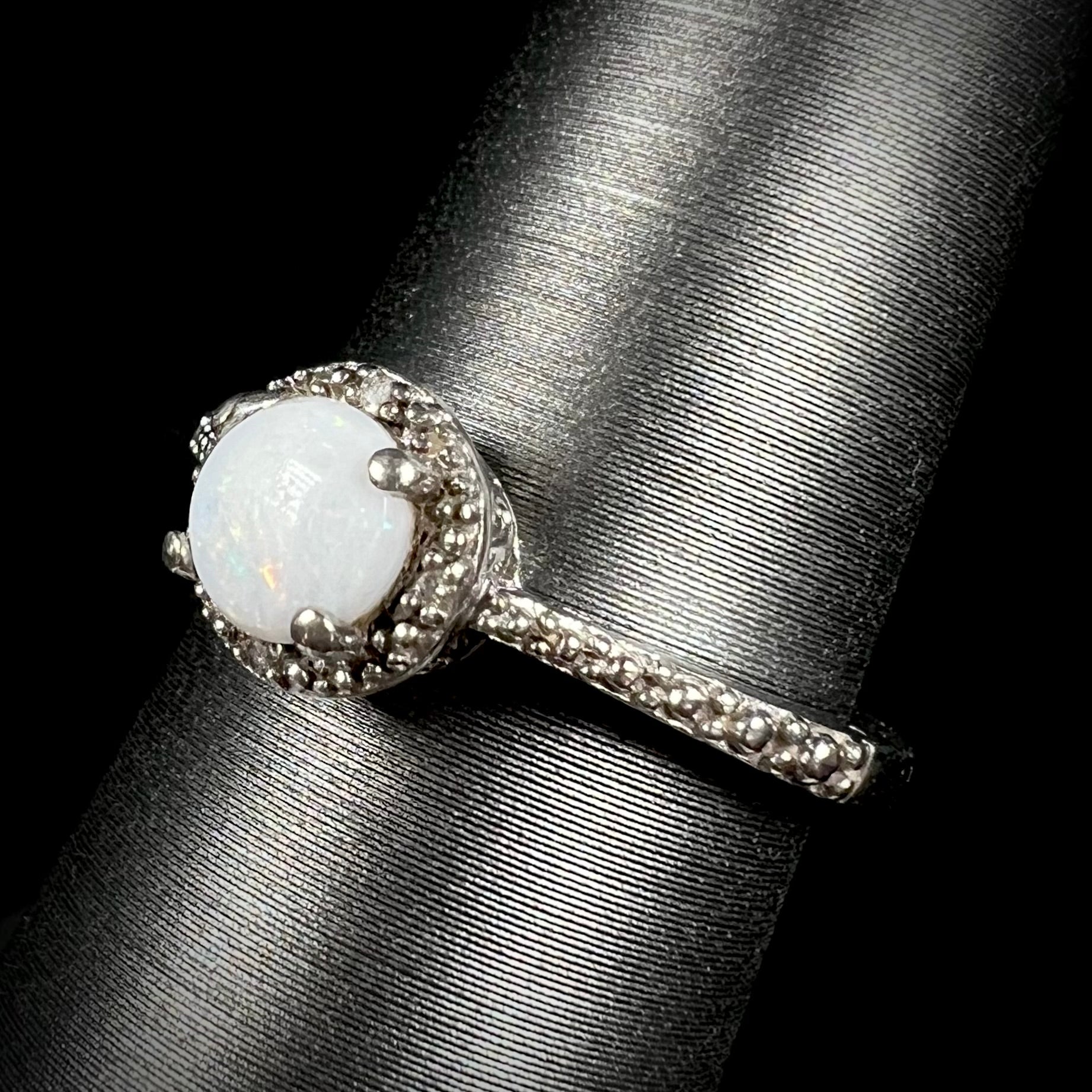 Angled view of a sterling silver white opal and diamond ring with a halo design.