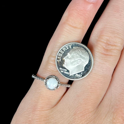 A sterling silver white opal and diamond ring with a halo design worn next to a 1997 S dime coin for scale.