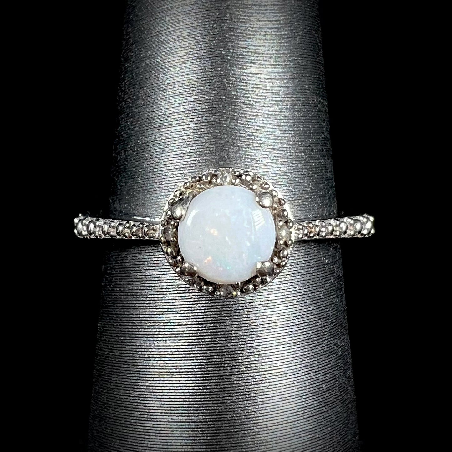 A sterling silver white opal and diamond ring with a halo design shown from the front against black background.