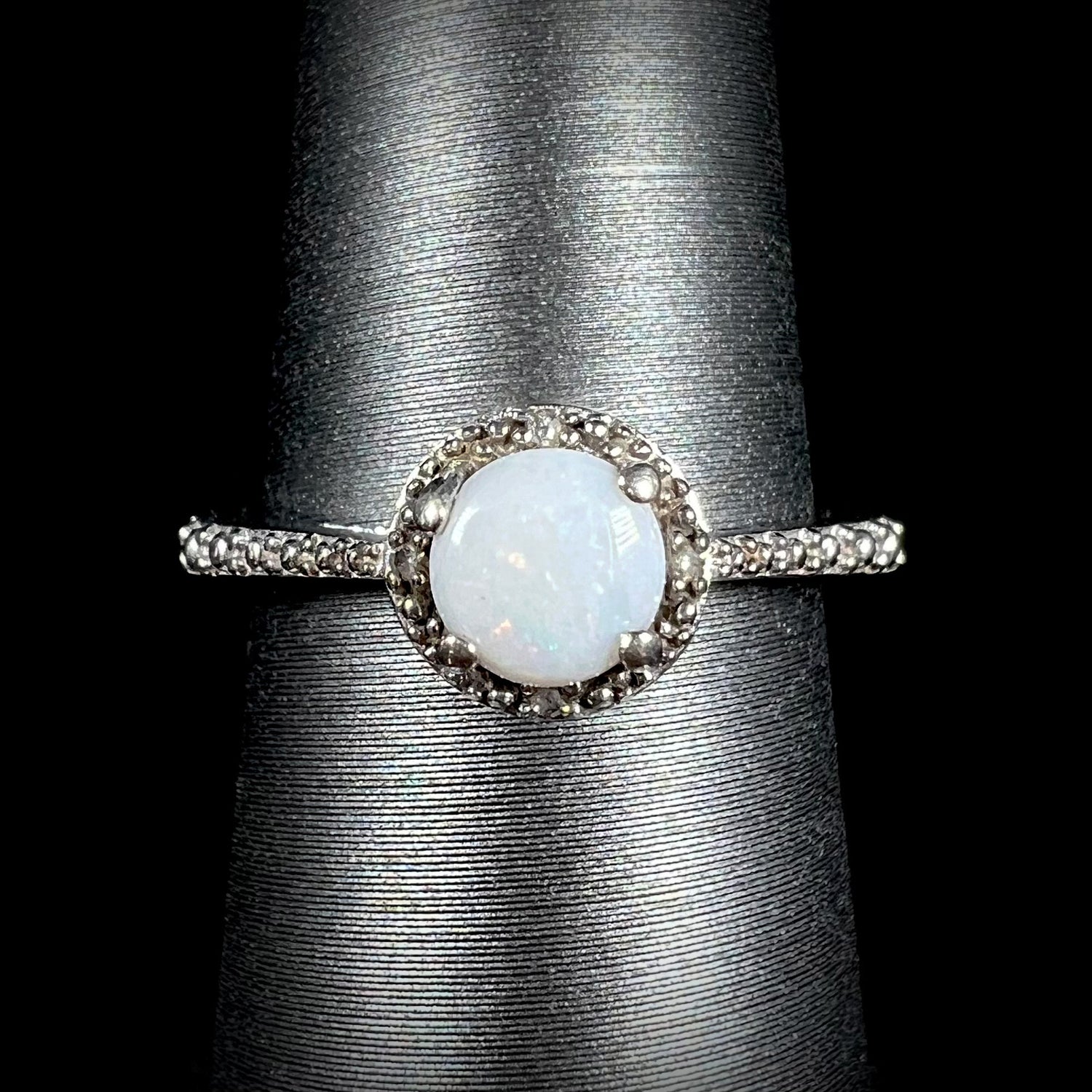 A sterling silver white opal and diamond ring with a halo design shown from the front against black background.