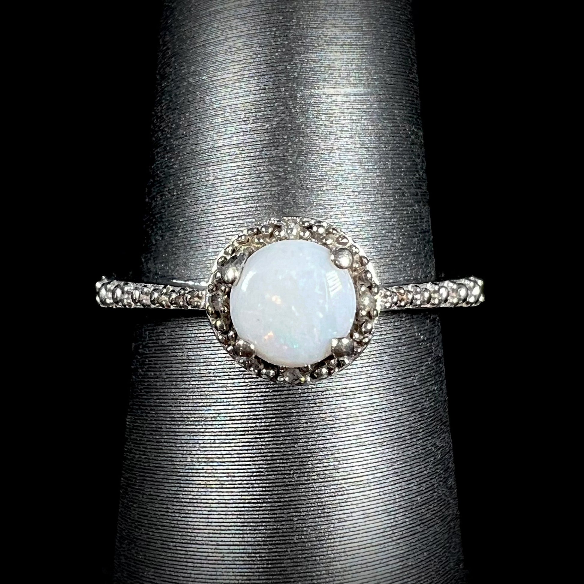 A sterling silver white opal and diamond ring with a halo design shown from the front against black background.