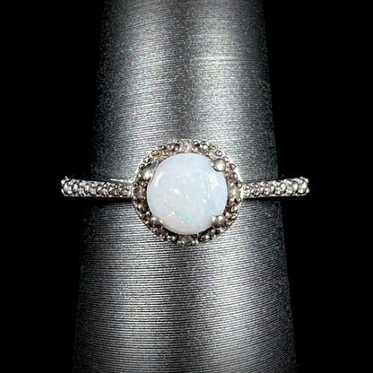 A sterling silver white opal and diamond ring with a halo design shown from the front against black background.