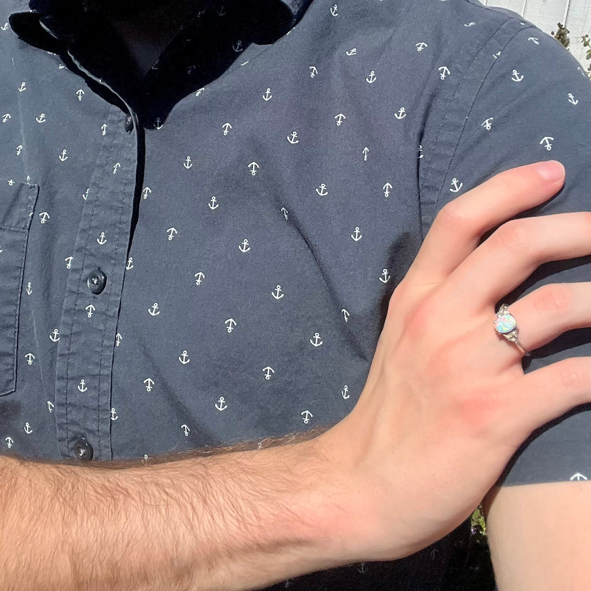Close-up of person resting hand on opposing shoulder in sunlight wearing a sterling silver lab-created opal and diamond women's ring.