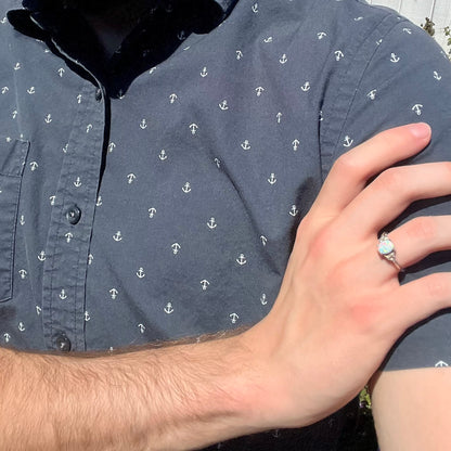 Close-up of person resting hand on opposing shoulder in sunlight wearing a sterling silver lab-created opal and diamond women's ring.
