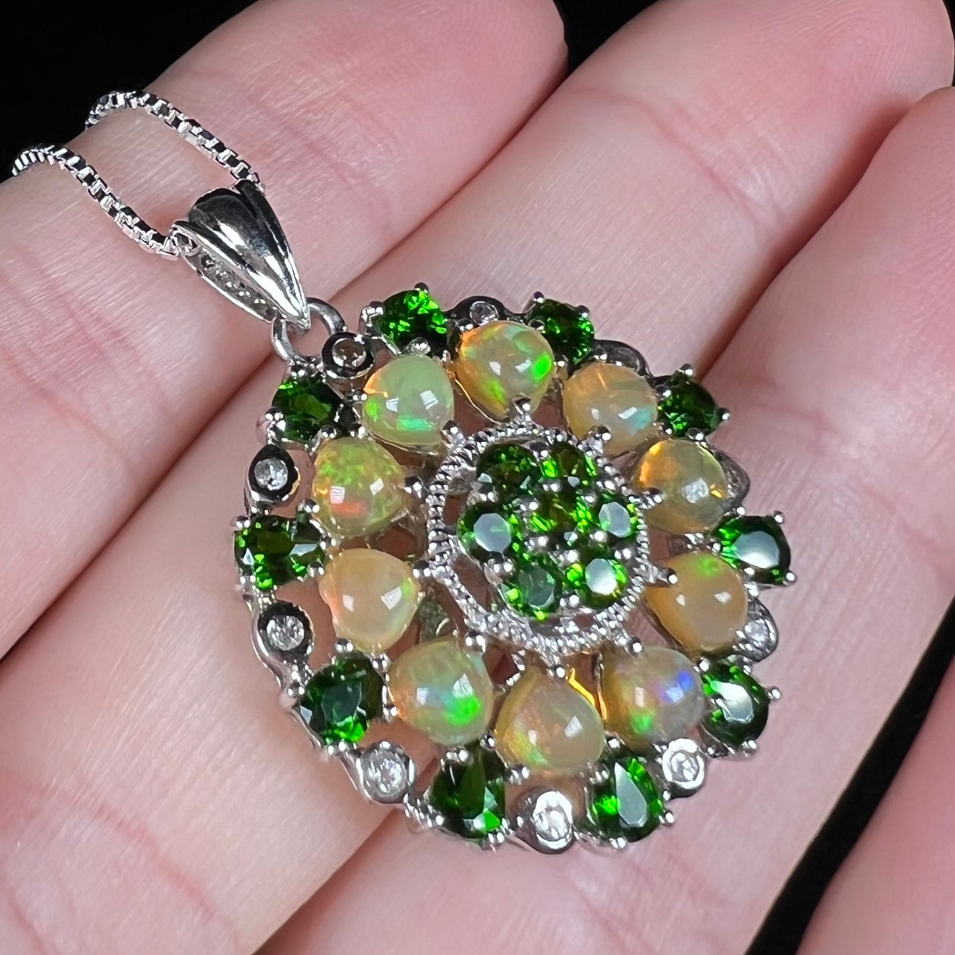 A silver Ethiopian opal and chrome diopside pendant held at an angle.