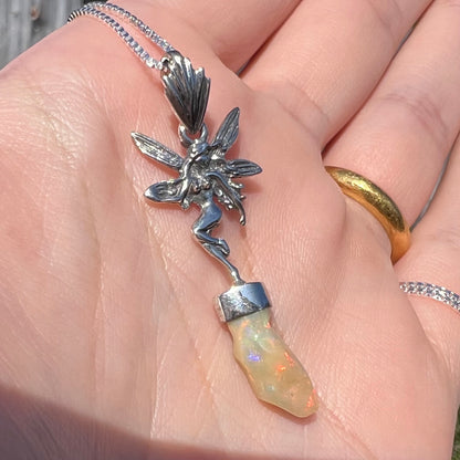 A sterling silver fairy necklace with an Ethiopian fire opal crystal, shown close-up at an angle in a hand in sunlight.