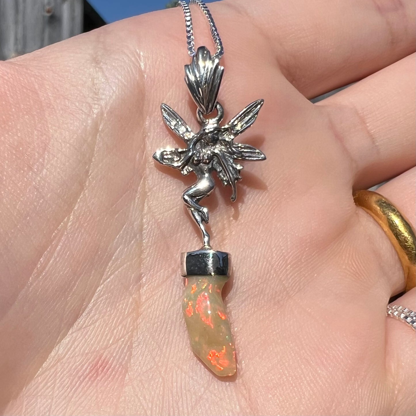 A sterling silver fairy necklace with a red Ethiopian fire opal crystal, shown close-up in a hand in sunlight.
