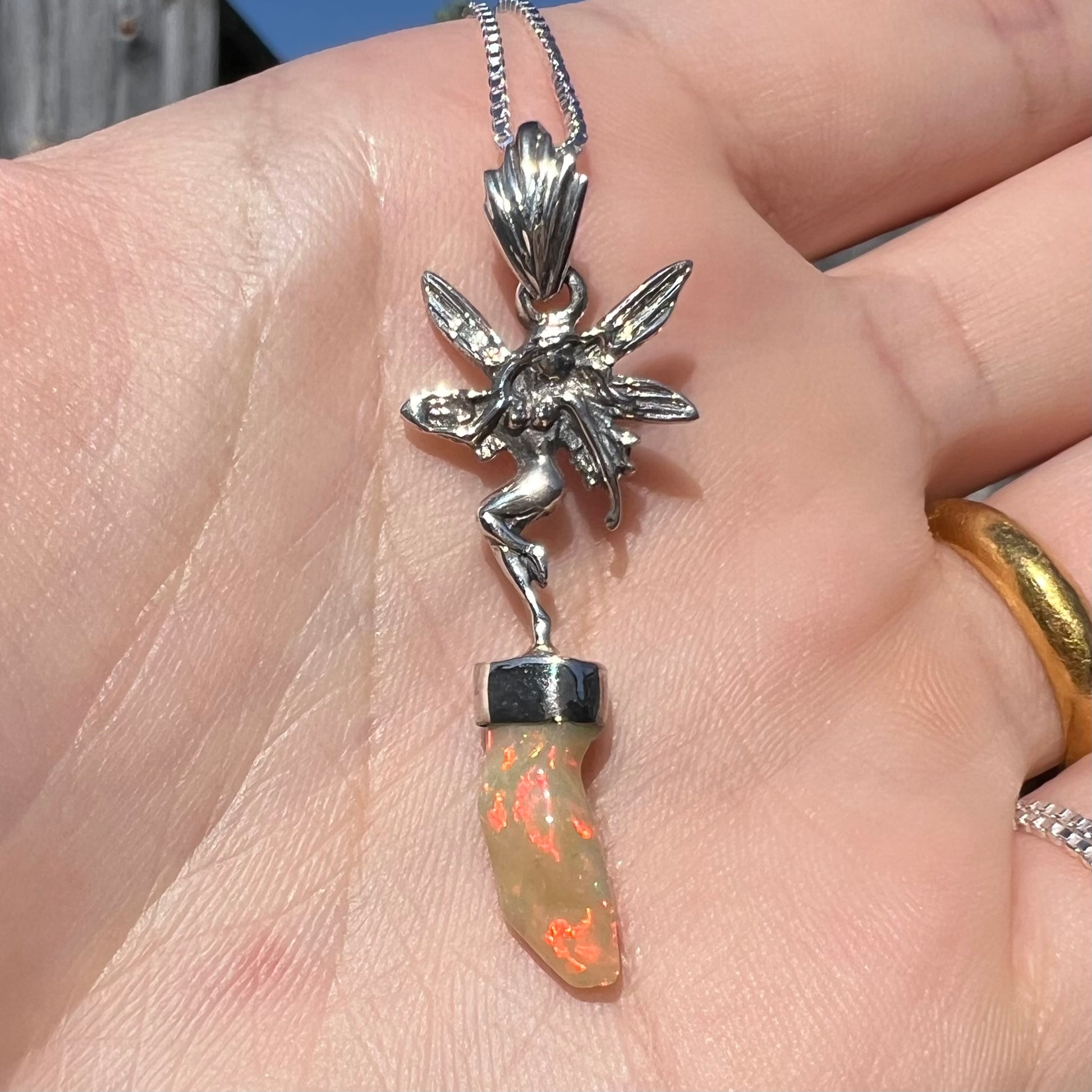 A sterling silver fairy necklace with a red Ethiopian fire opal crystal, shown close-up in a hand in sunlight.