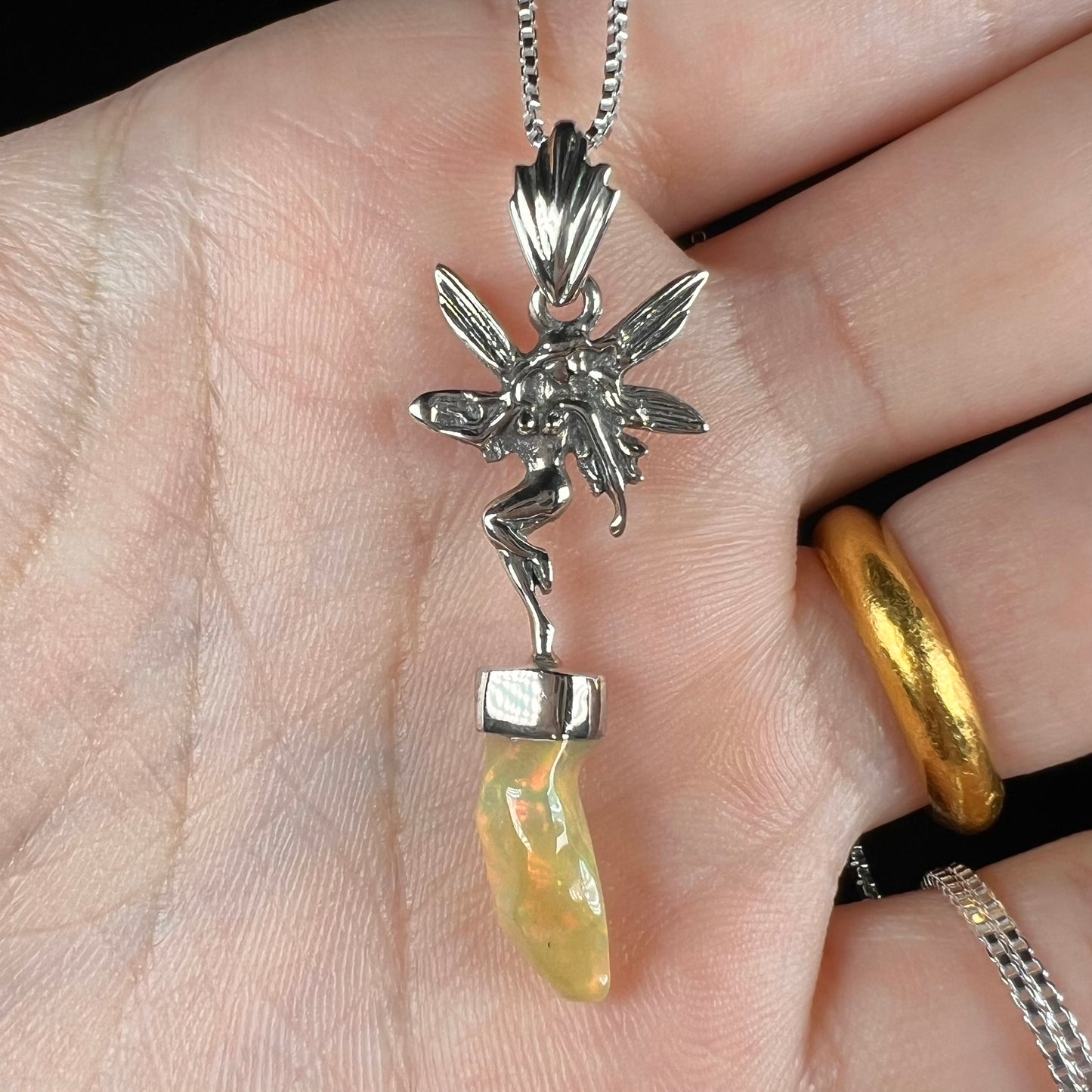 A sterling silver fairy necklace with an Ethiopian fire opal crystal, shown close-up in a hand.