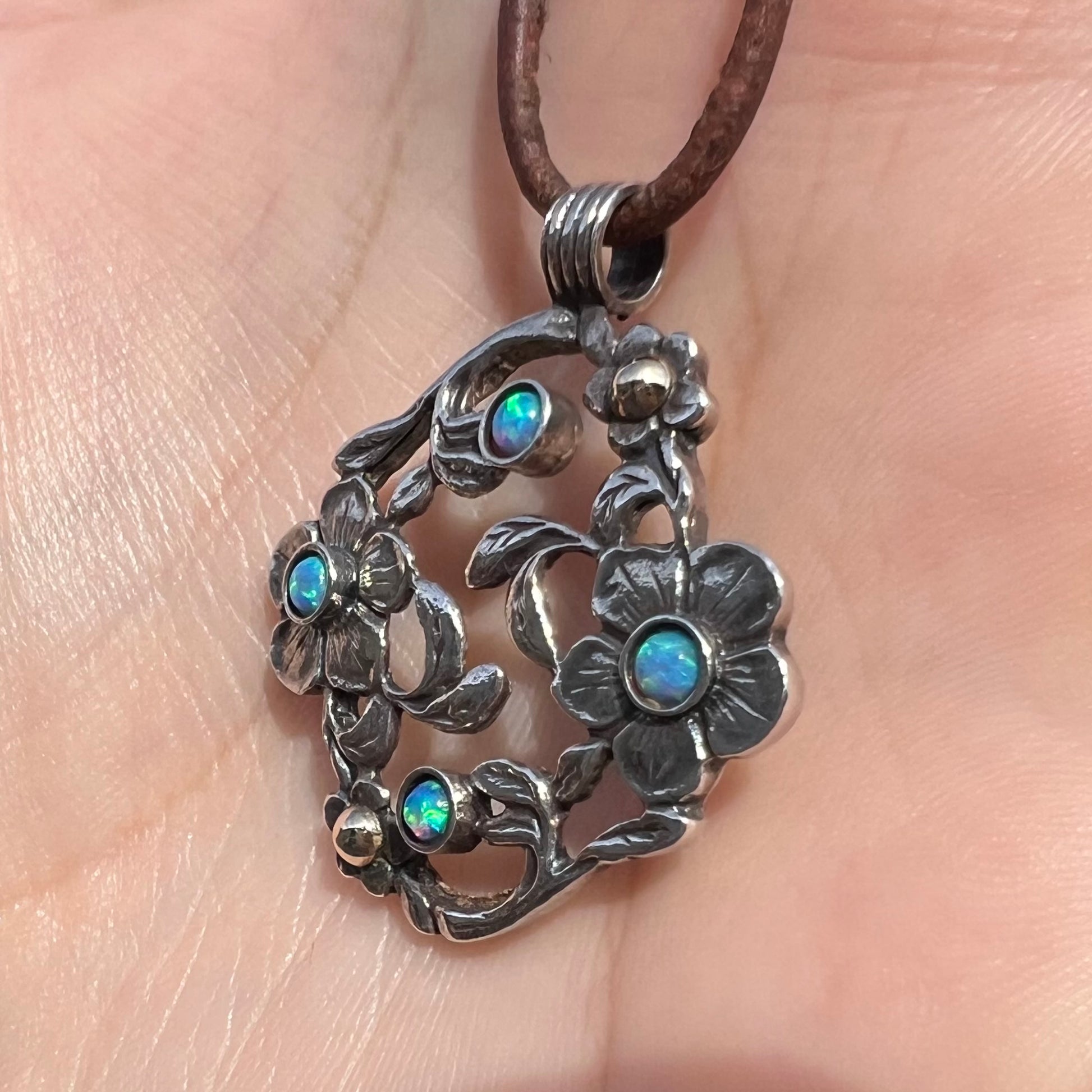 A two-tone sterling silver and 14k gold opal dogwood flower pendant shown in a hand from an angle in sunlight.