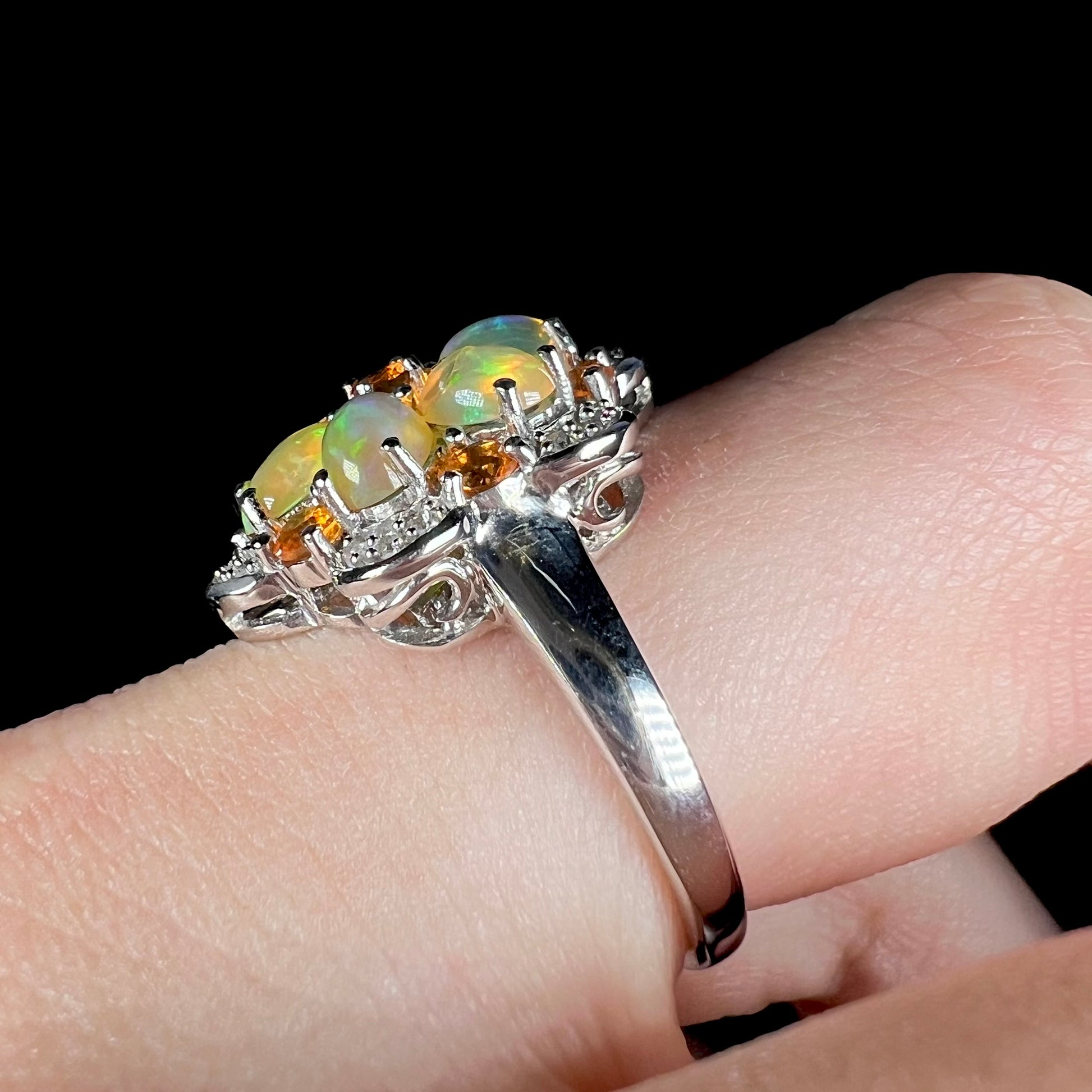The side of a silver opal flower ring worn on a finger, focused on an eye-visible scratch on the ring's shank.