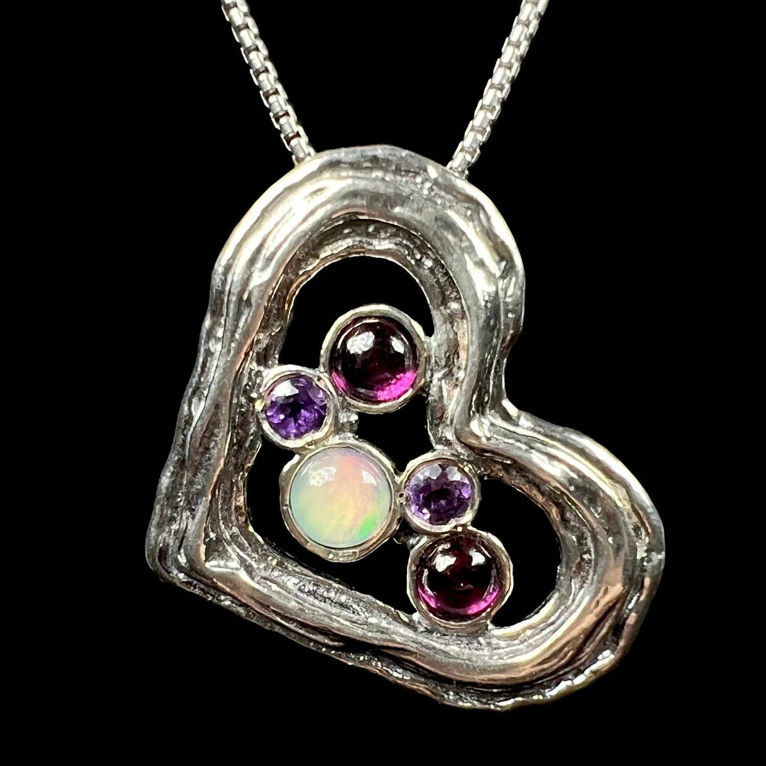 A sterling silver heart necklace set with a round Ethiopoian opal, two amethysts, and two rhodolite garnets.