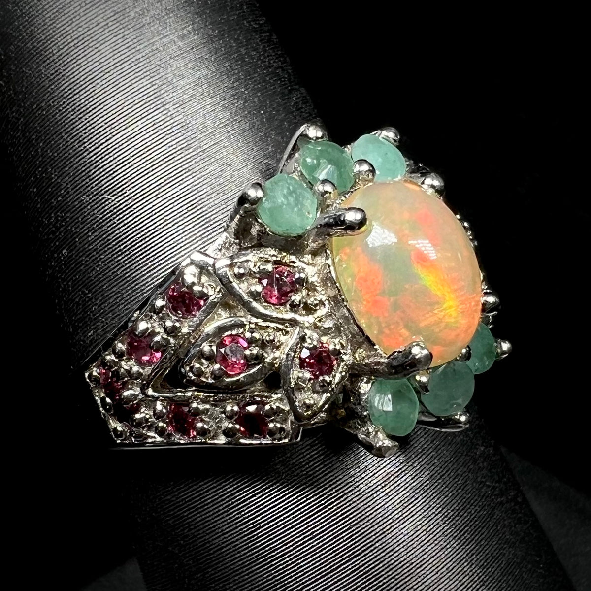 Angled close-up of sterling silver opal, garnet, and emerald ring on ring display