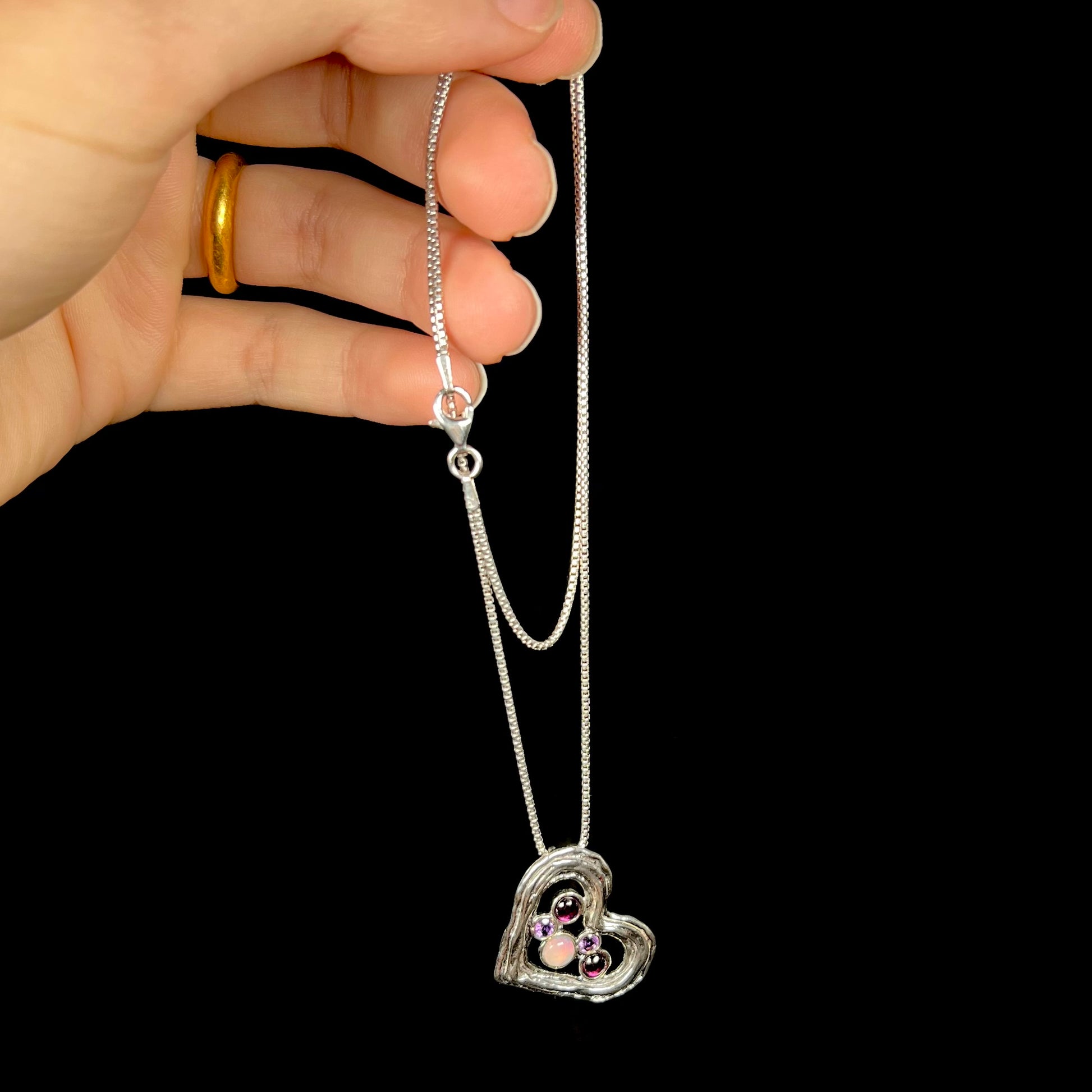 A sterling silver heart necklace set with a round Ethiopoian opal, two amethysts, and two rhodolite garnets.