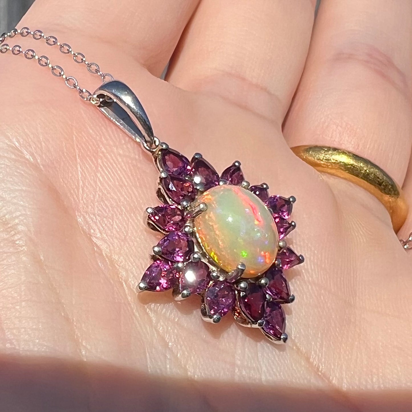 Angled close-up of a sterling silver Ethiopian opal and rhodolite garnet spray necklace in sunlight, held in hand.