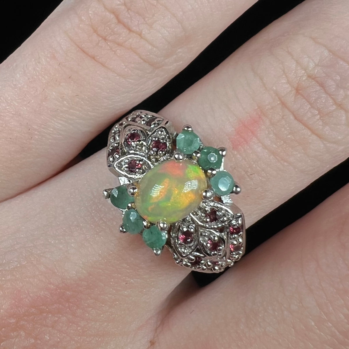 Close-up of sterling silver Ethiopian fire opal ring with green beryl and garnet accents, worn on finger