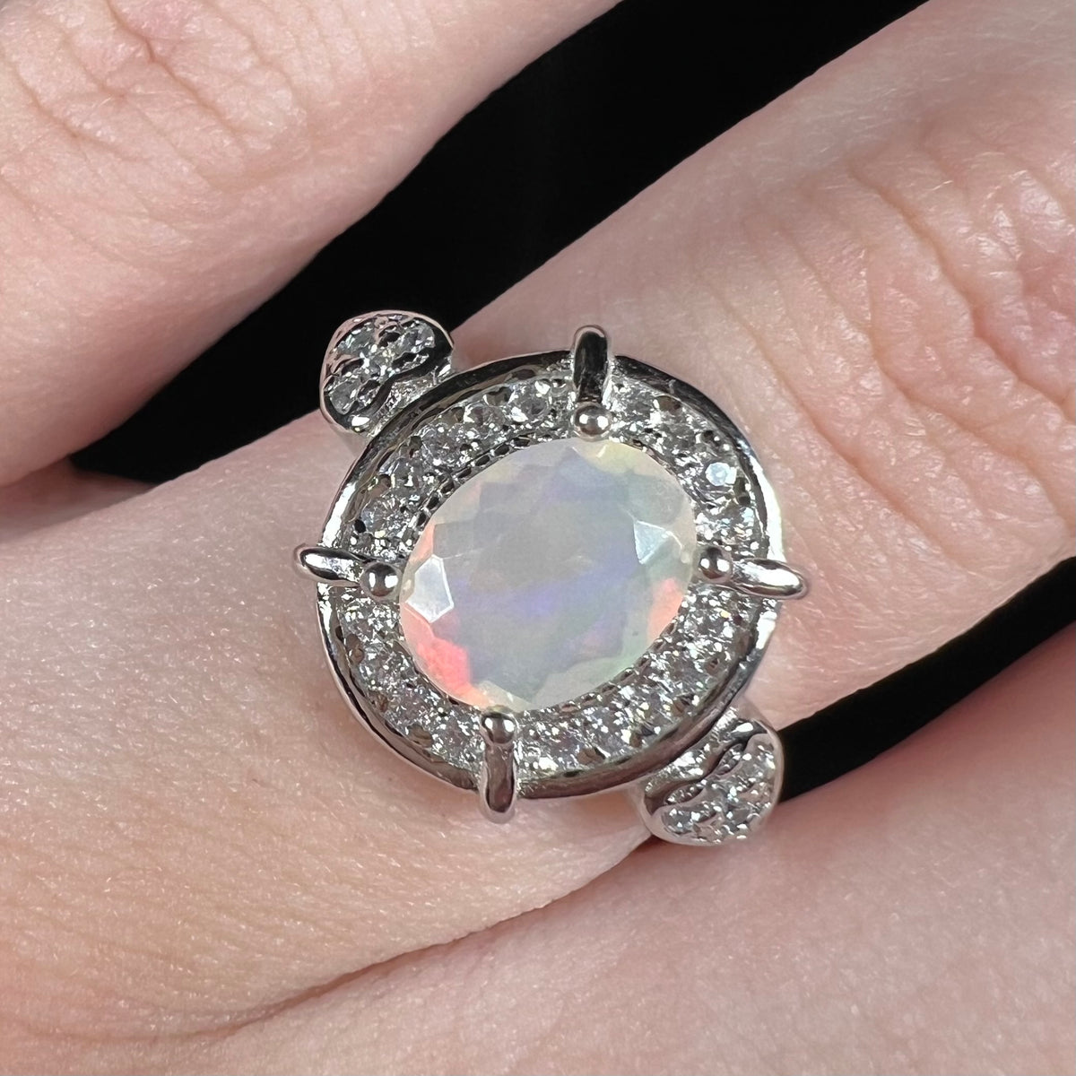 Close-up of silver Ethiopian opal and CZ halo ring with heart design accents worn on finger