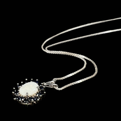 An angled view of a silver opal halo necklace lying on a black background, showcasing its dainty prong setting.