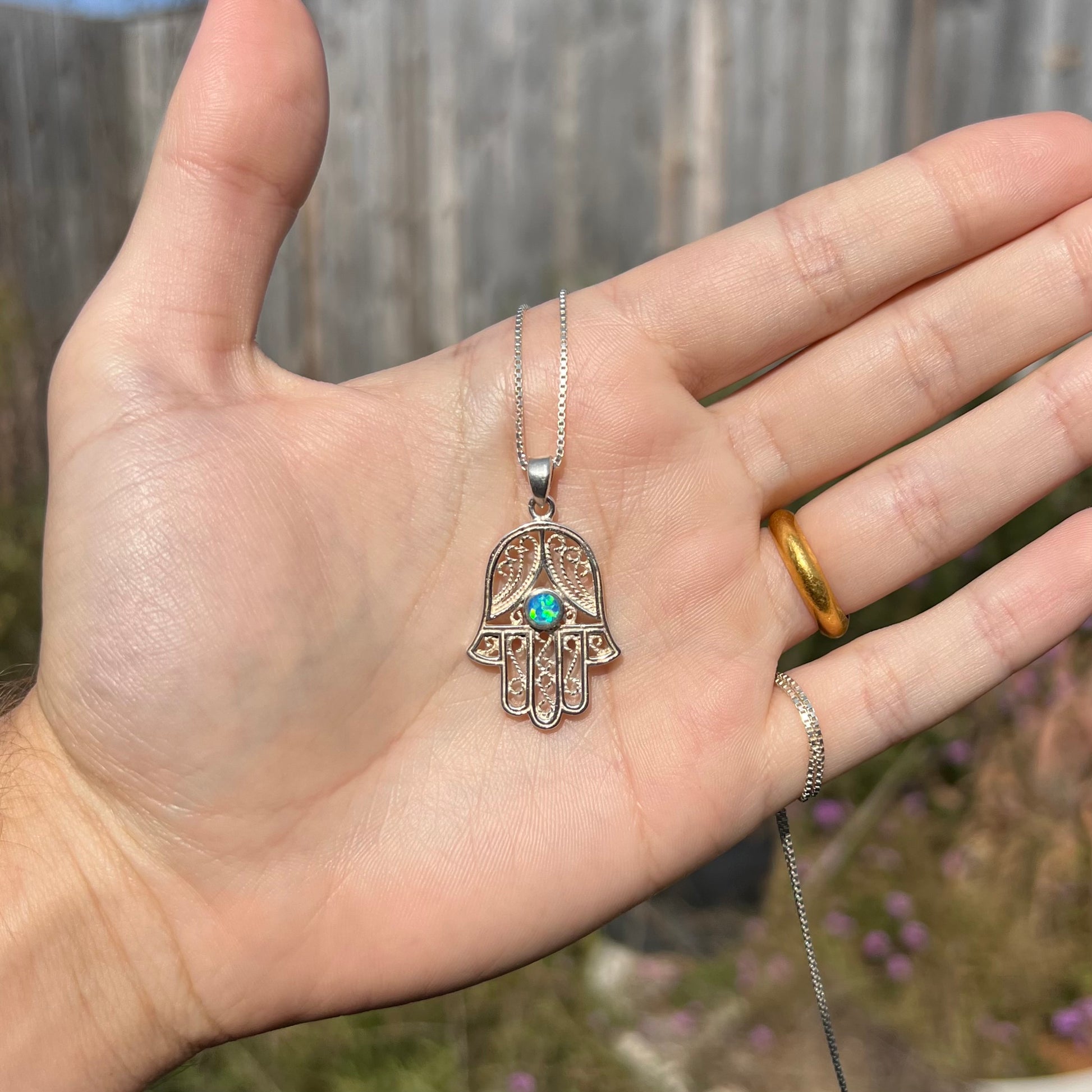 A sterling silver and filigree-accented hamsa hand necklace set with a round lab-created opal.