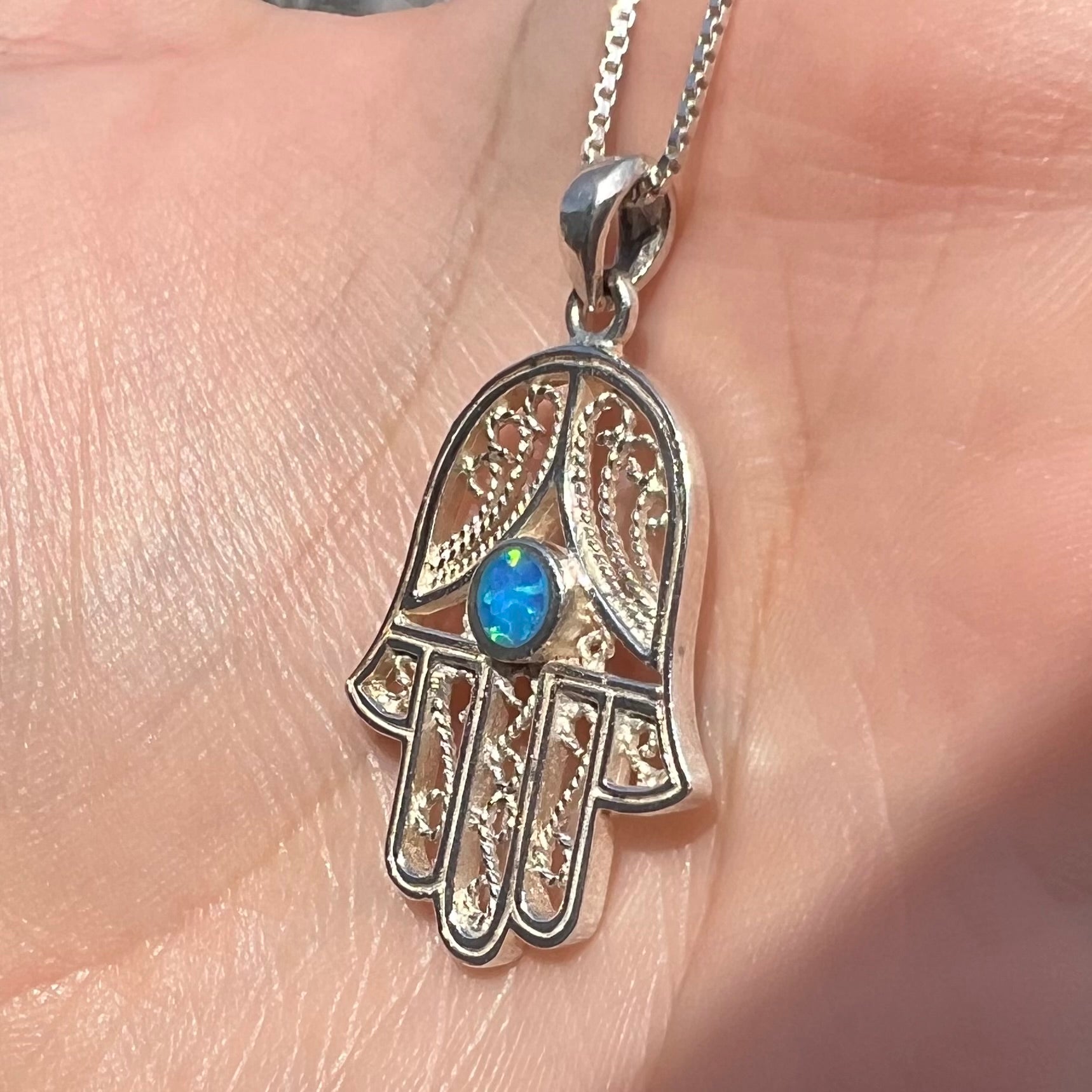 A sterling silver and filigree-accented hamsa hand necklace set with a round lab-created opal.