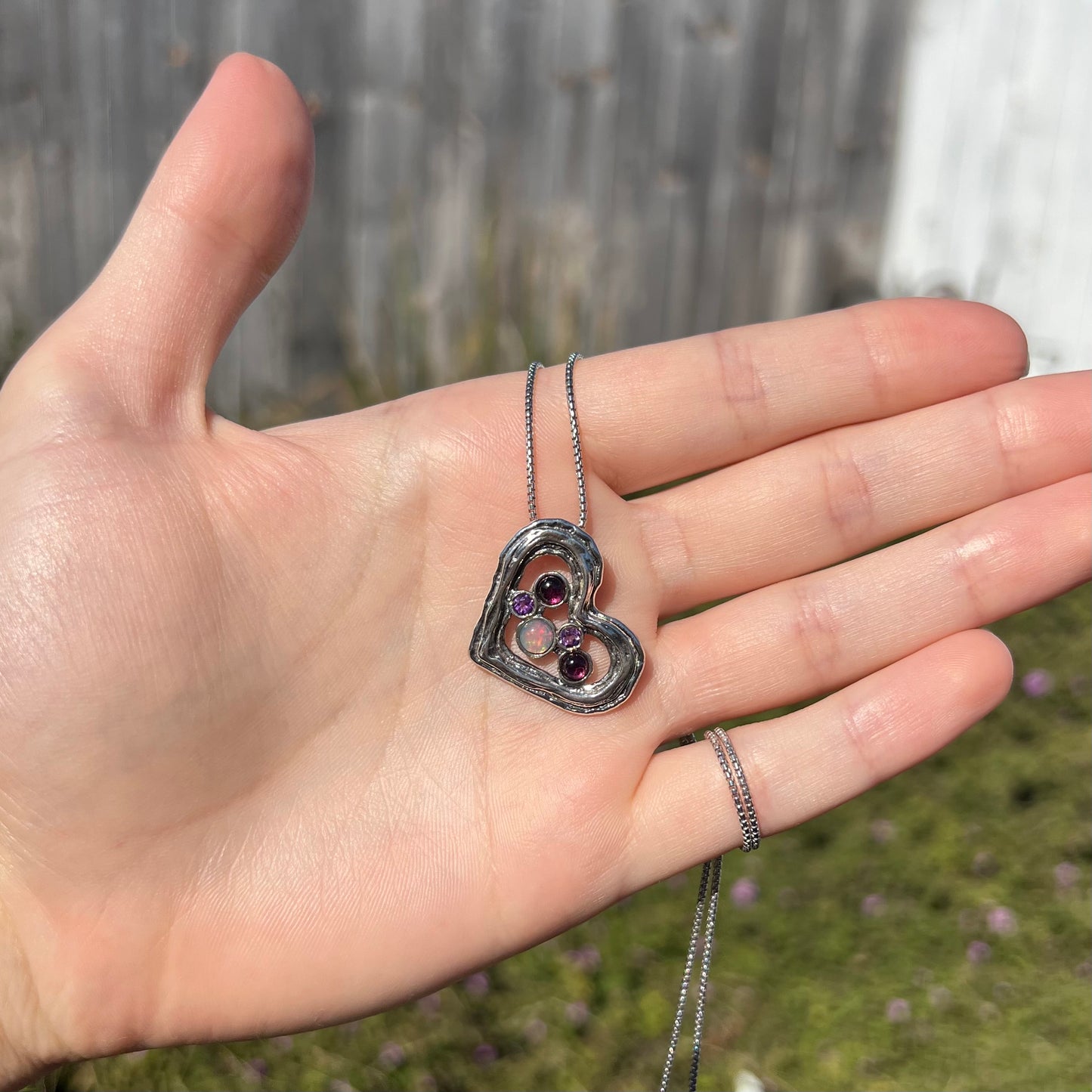 A sterling silver heart necklace set with a round Ethiopoian opal, two amethysts, and two rhodolite garnets.