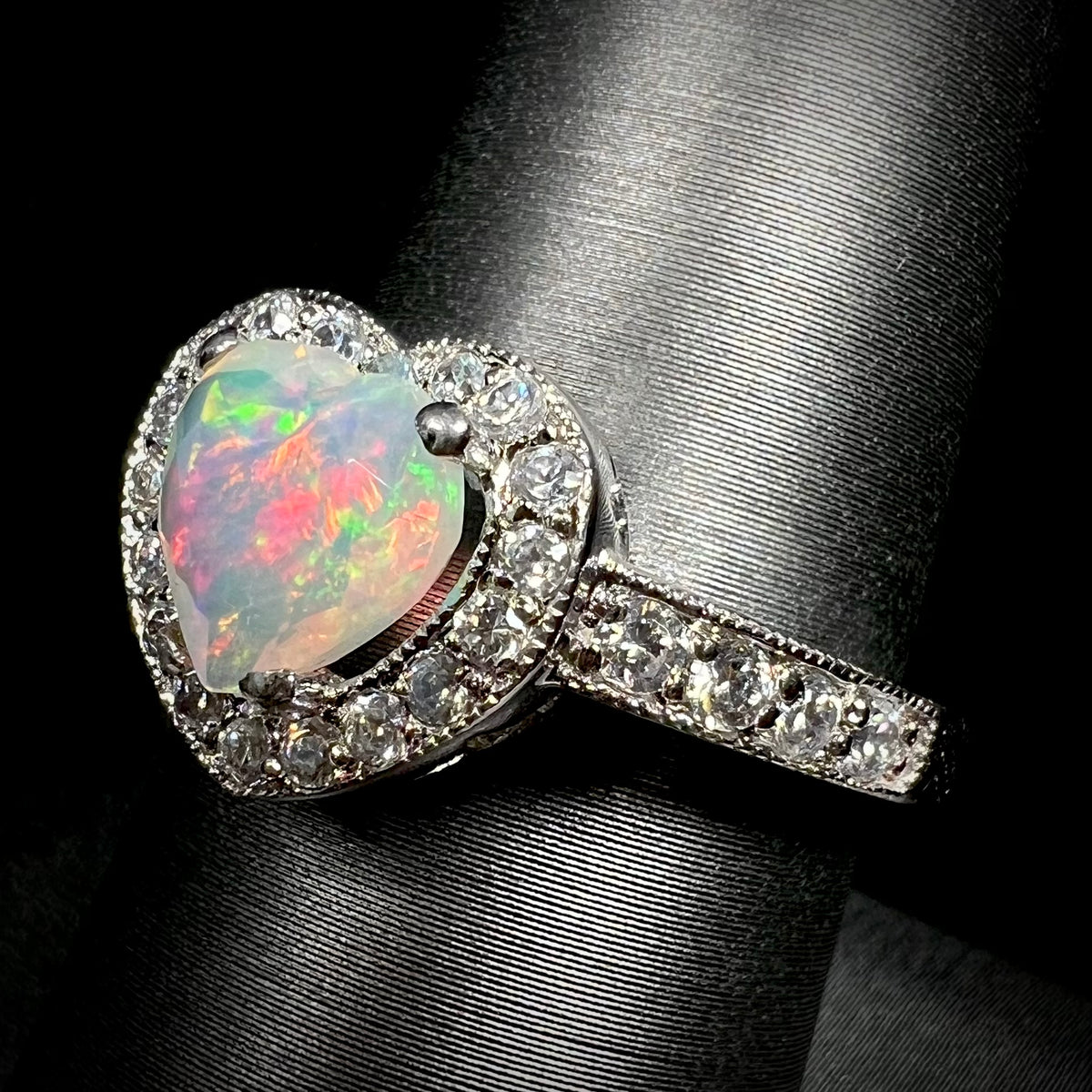 Macro angled view of sterling silver opal heart ring with pave set cubic zirconia accents, shown on ring display