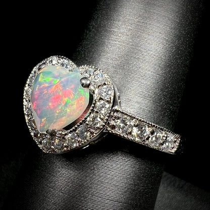 Macro angled view of sterling silver opal heart ring with pave set cubic zirconia accents, shown on ring display
